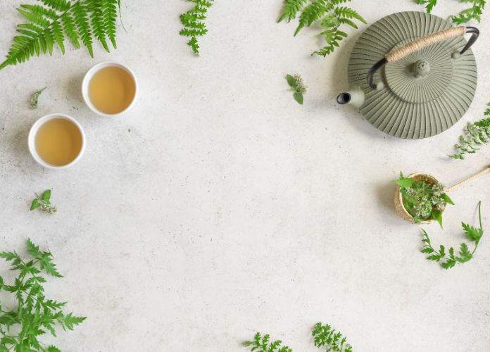 Herbal tea with teapot and fresh herbs on a light background.