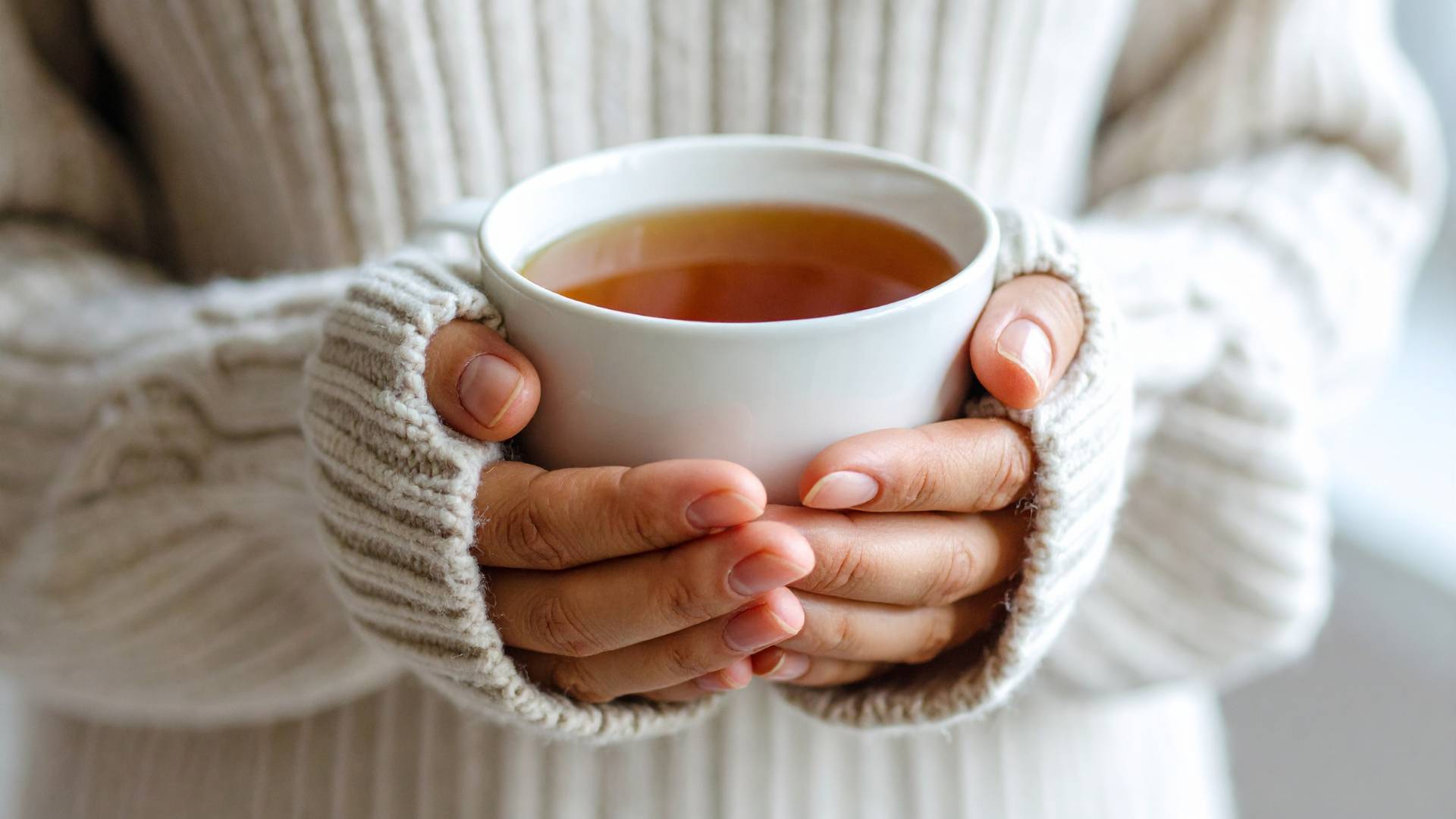 Person holding a warm cup of herbal tea for detox support in cozy sweater.