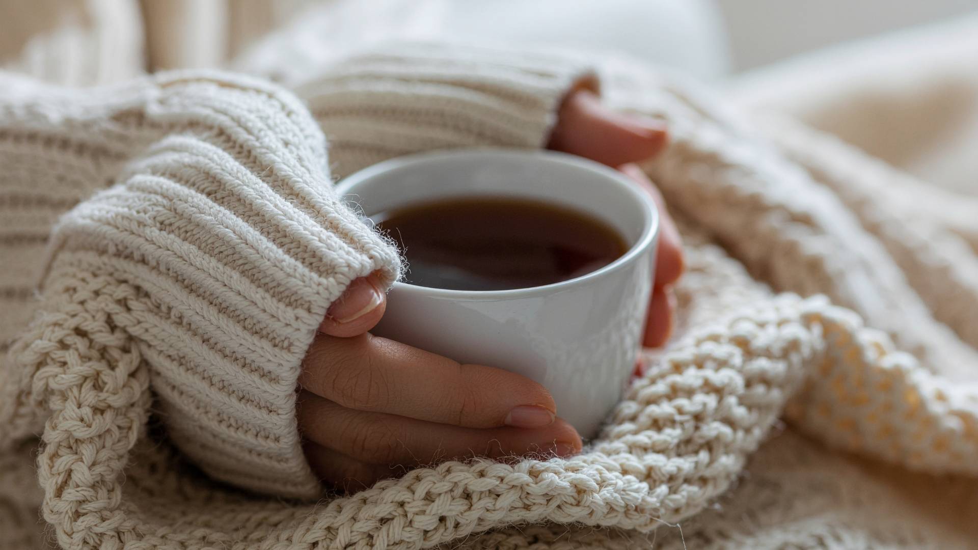 Person holding a warm cup of herbal tea while wrapped in a cozy blanket, calming herbal tea for night relaxation support