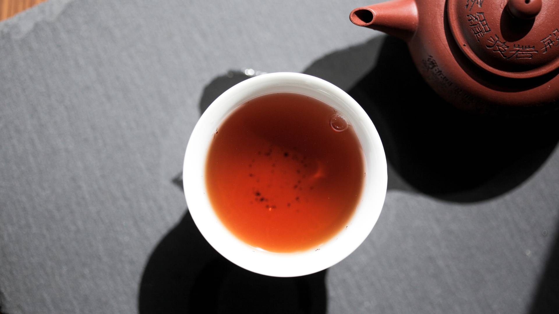 Cup of herbal tea with teapot on dark surface, soothing herbal tea for indigestion support