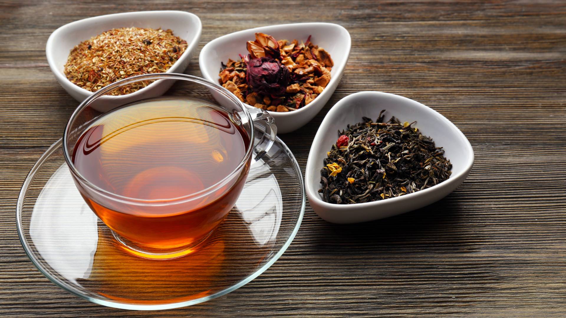 Cup of herbal tea with assorted dried herbs in bowls on wooden table, Herbal Tea for Bloating support