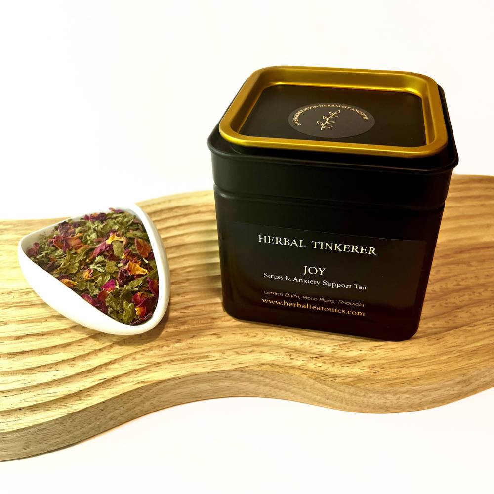 Joy blend in black tin with loose herbs on wooden board, herbal tea for stress support