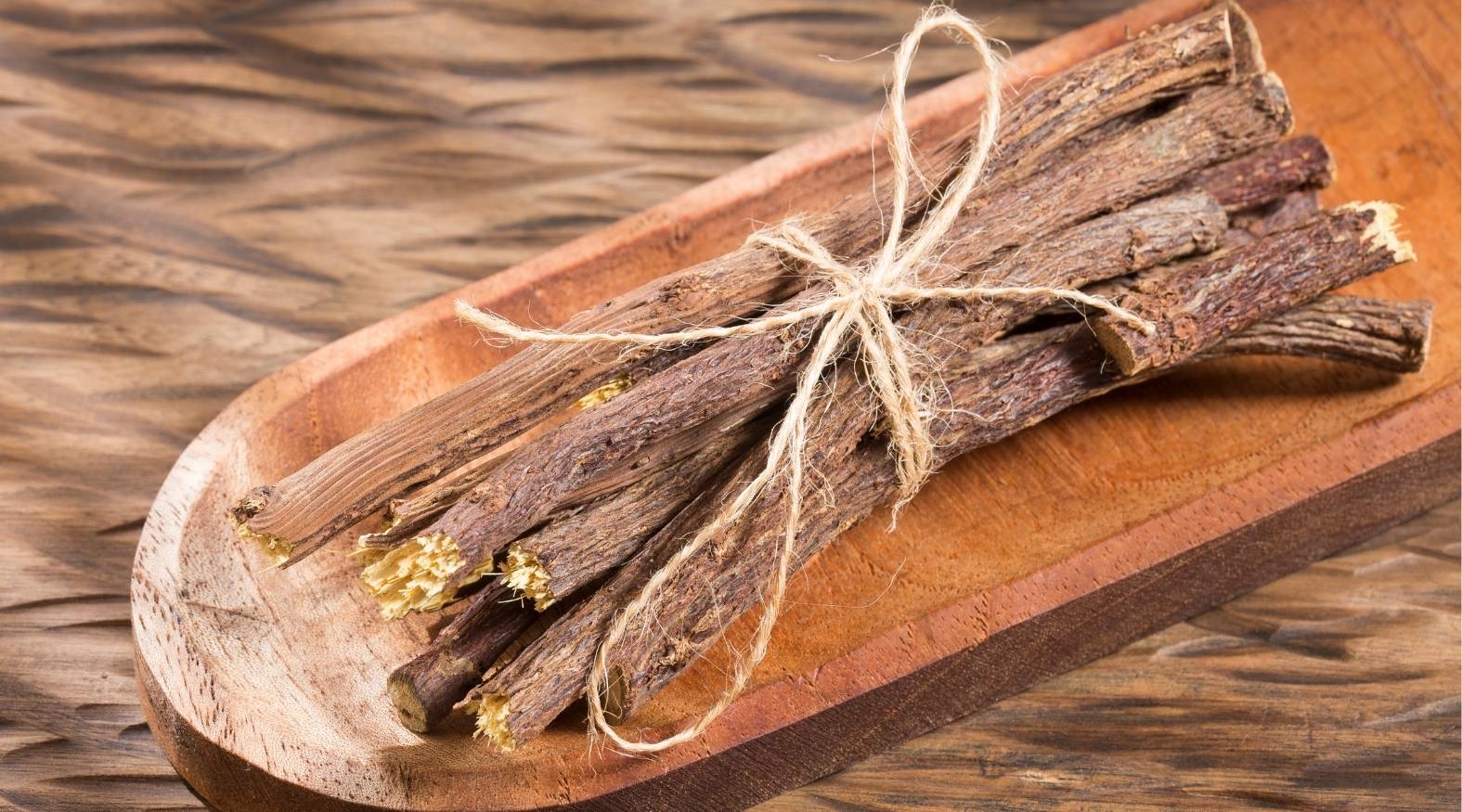 Licorice root (Glycyrrhiza glabra) showing dried, woody root sticks bundled together, with rough textured surfaces and natural brown tones displayed on a wooden tray.