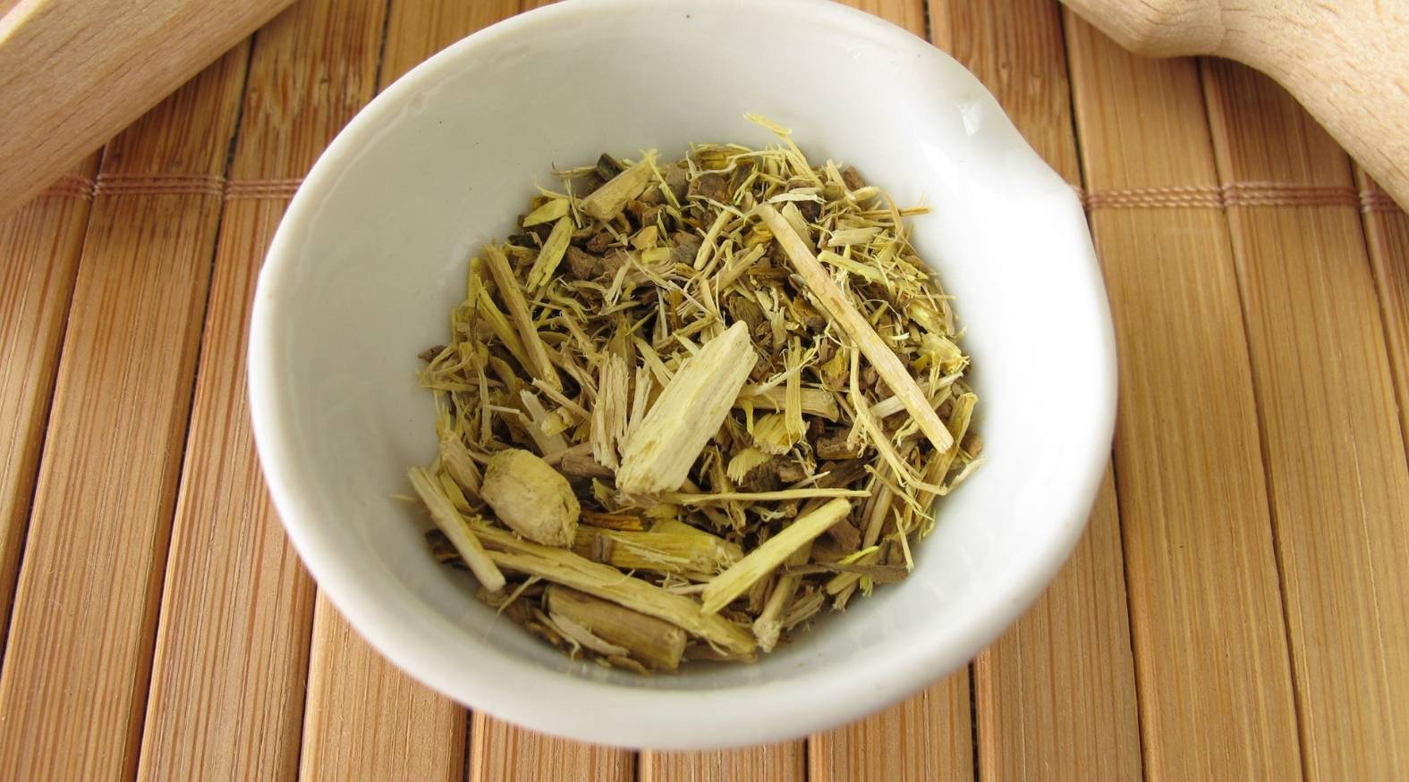 Close-up of Oregon grape root (Mahonia aquifolium) showing dried, chopped root pieces with a distinctive yellow interior, arranged in a small white bowl on a natural wooden surface.