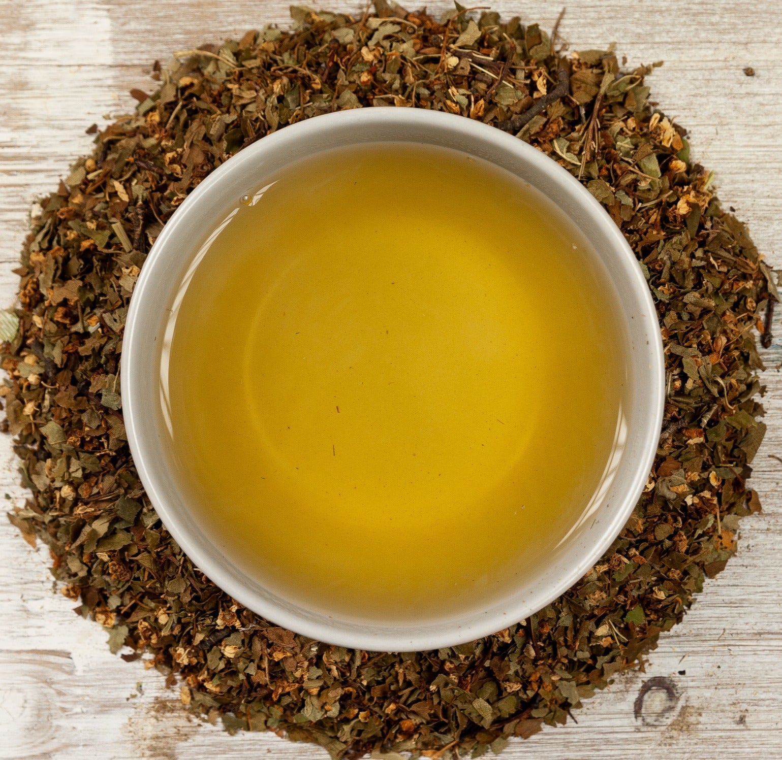 Cup of golden herbal tea surrounded by dried herbs, a herbal tea for inflammation support