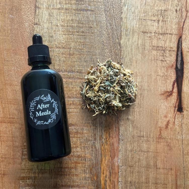 Black bottle labeled 'After Meals' next to dried herbs on a wooden surface