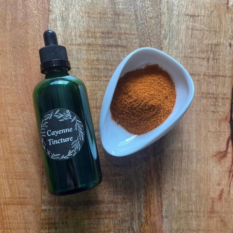Cayenne Tincture bottle next to a bowl of cayenne pepper on a wooden surface