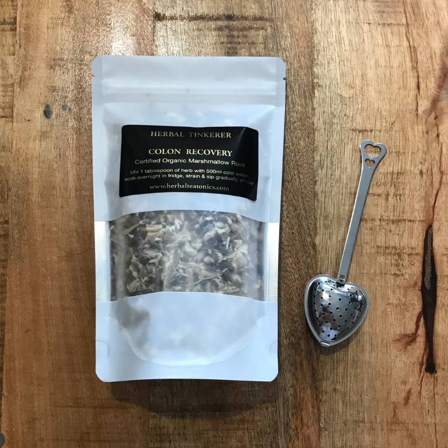 Herbal tea package labeled 'Colon Recovery' with a metal tea scoop on a wooden surface