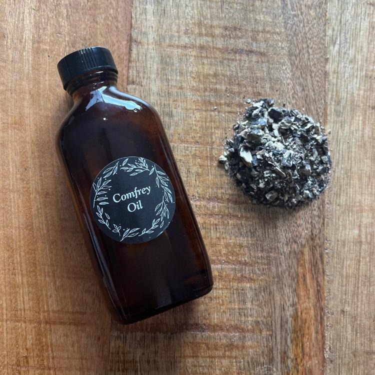 Brown bottle labeled 'Comfrey Oil' next to a rock on a wooden surface