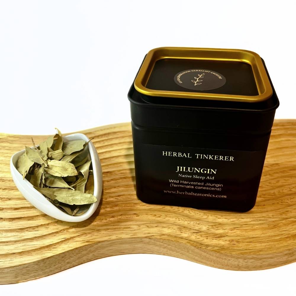 Black tin labeled 'Herbal Tinkerer' with dried herbs on a wooden board
