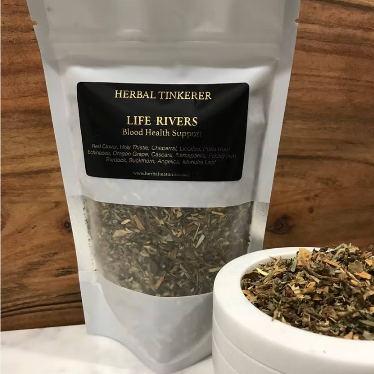 Herbal tinkerer product packaging with dried herbs on a wooden surface