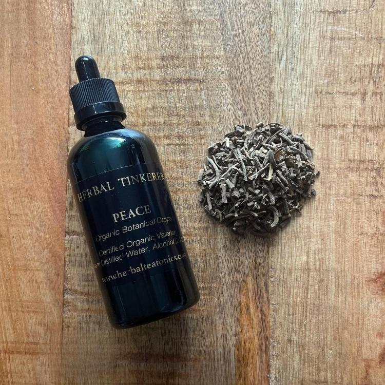 Bottle labeled 'Herbal Tinkering' with 'Peace' on a wooden surface, next to a ball of dried herbs.