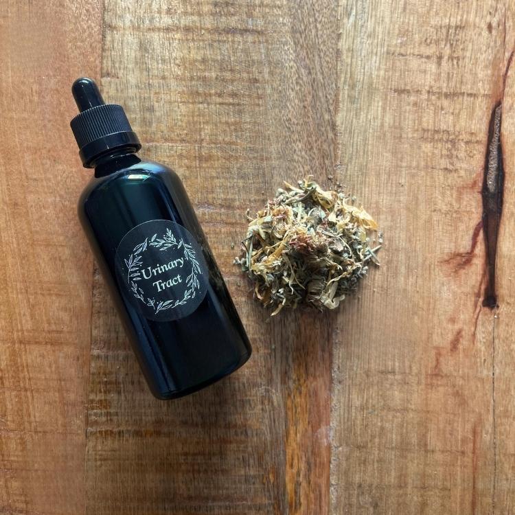 Black bottle labeled 'Urinary Tract' next to a ball of dried herbs on a wooden surface