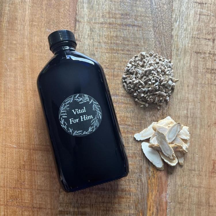 Black bottle labeled 'Vital For Him' on a wooden surface with dried herbs.
